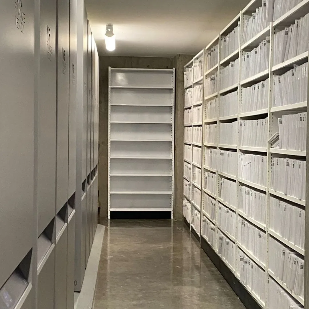 Pasillo de archivo con estantería móvil compacta a un lado y estantería fija cargada de expedientes al otro