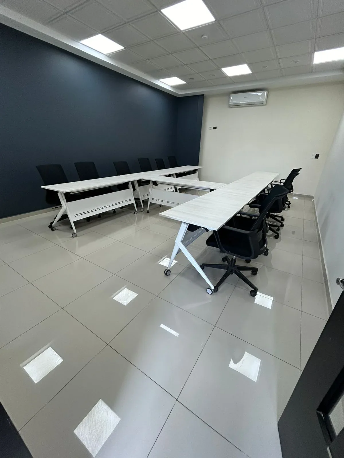 Sala de capacitación con mesas plegables en U y sillas de malla negras