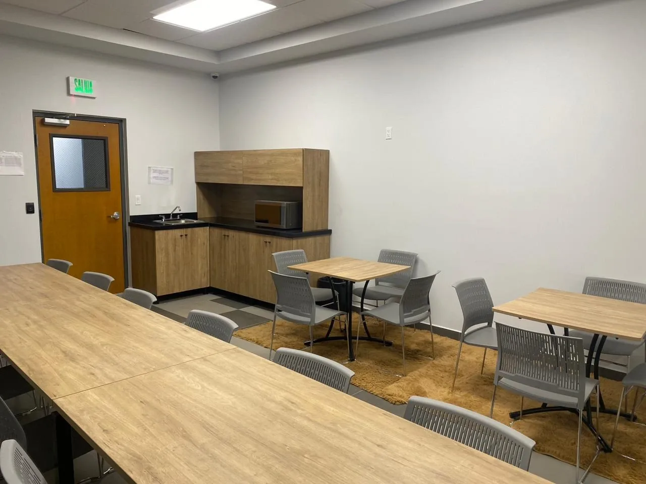 Comedor de empresa con mesas corridas, mesas para cuatro y cocineta de melamina al fondo
