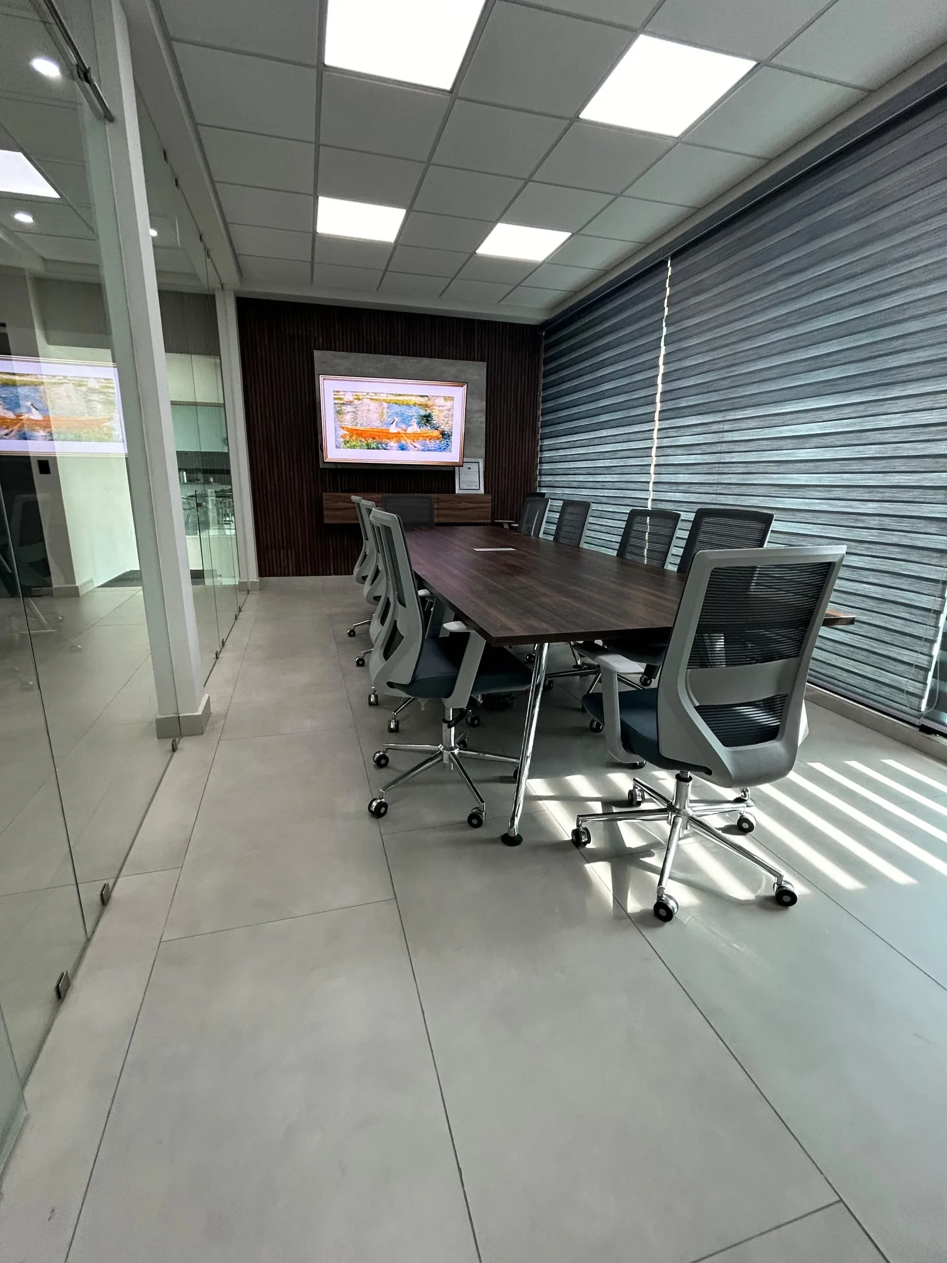 Sala de juntas con mampara de cristal, mesa larga de madera y sillas giratorias de malla