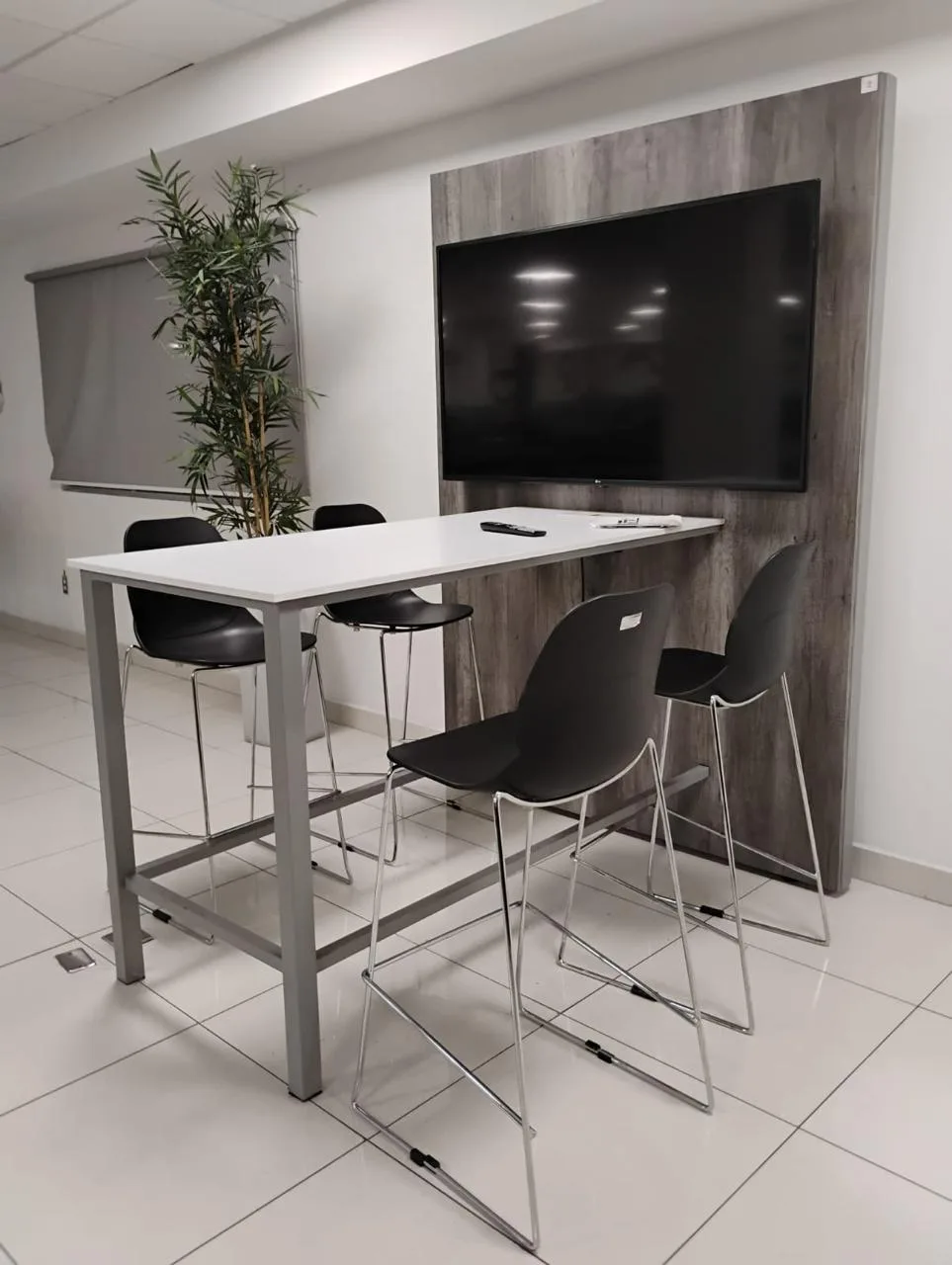 Mesa alta con bancos frente a pantalla, sobre panel de madera, para reuniones cortas